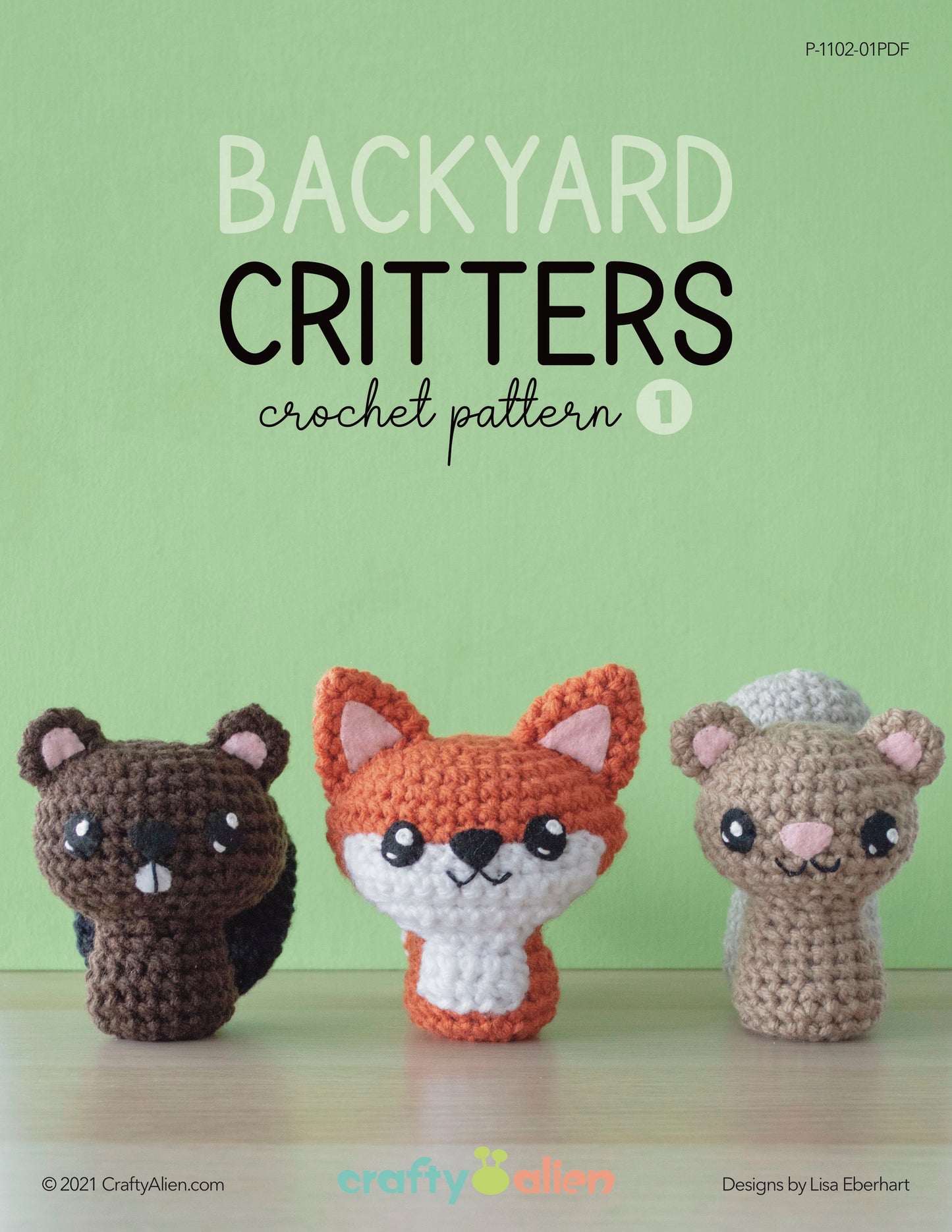 Three crochet amigurumi figures rest on a wooden surface with a green backdrop. From left to right, meet the brown bear, orange fox, and gray raccoon. This wild whimsy collection is titled Backyard Critters Crochet Pattern 1 by CraftyAlien and Lisa Eberhart.